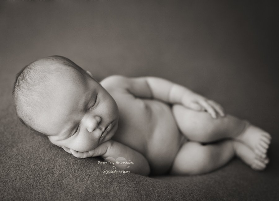 sort hvid billede af nyfødt liggende på siden med hånden under kinden på tæppe - sort hvid