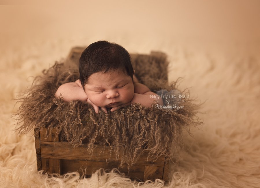 nyfødt foto af dreng sovende med brunt tæppe i trækasse