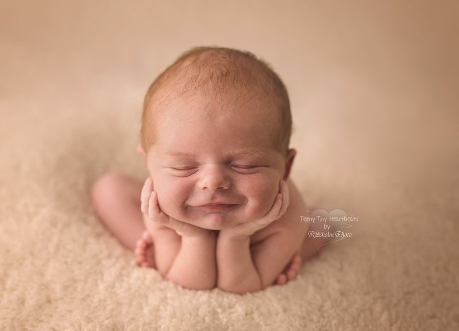 billede af smilende sovende nyfødt med hænderne under hagen i creme farve
