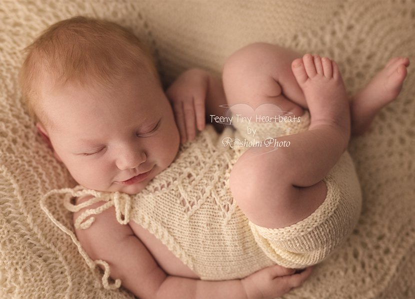 foto af smilende nyfødt i hvid dragt liggende på ryggen