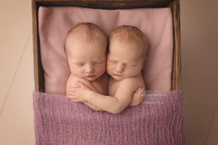 billede af nyfødte sovende tvillingepiger i trækasse med lyserødt tæppe