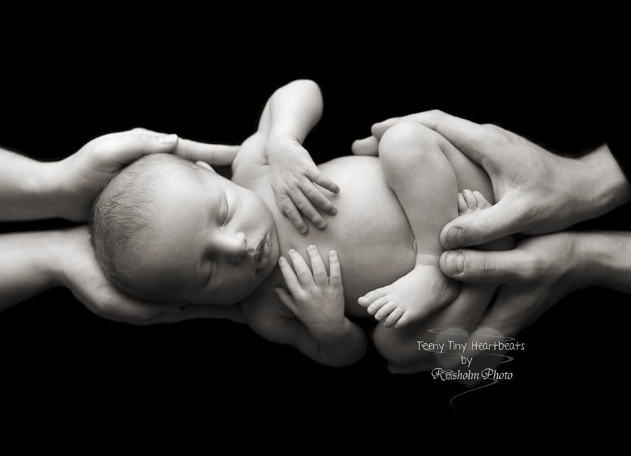 foto af nyfødt sovende i mors og fars hænder med sort stofbaggrund i sort hvid