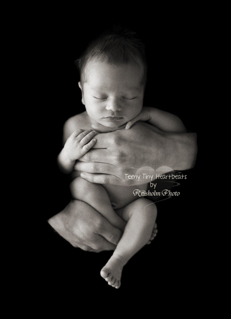 sort hvid billede af sovende nyfødt i fars hænder med sort baggrund